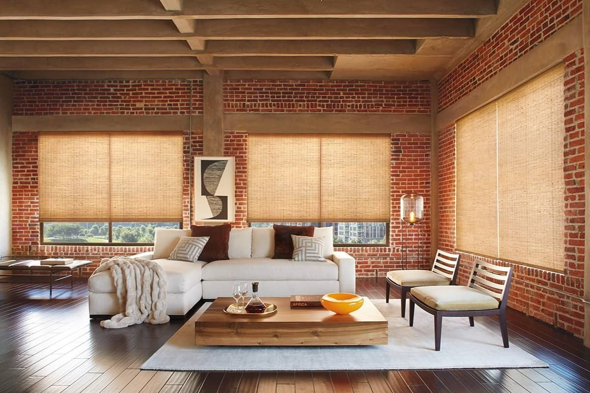 Hunter Douglas Provenance® Woven Wood Shades in a living room with an exposed brick wall